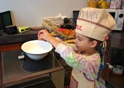 Enfant en tablier cassant un œuf dans un bol.